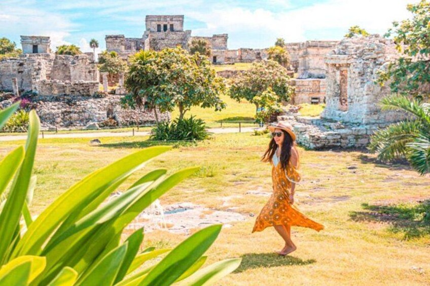 A woman in a yellow dress walking in a grassy area with ancient ruins in the background. 5