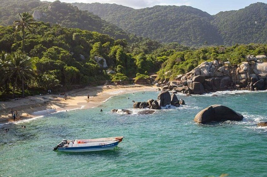 En båd på en turkis strand med klippeformationer og frodig vegetation i baggrunden. 2