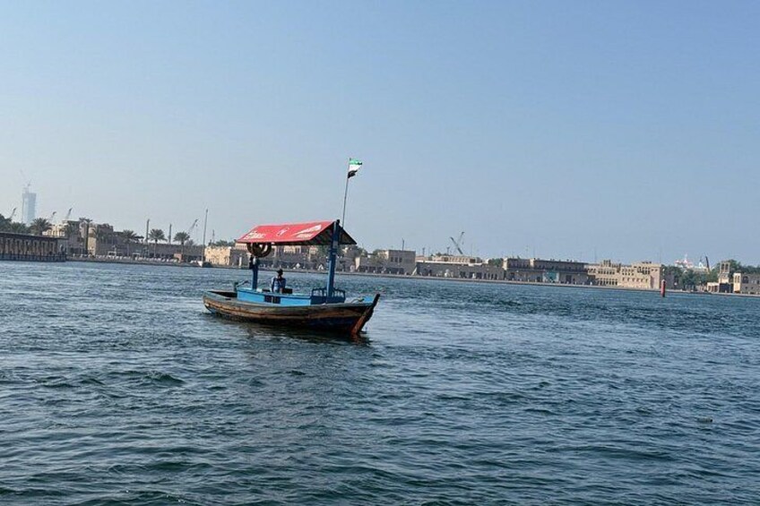 Un bote con toldo rojo sobre agua, una orilla distante con edificios y un cielo despejado. 5