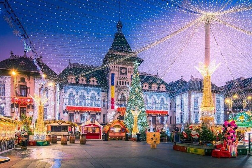 A festive square with illuminated buildings, a large Christmas tree, and a Ferris wheel. 1