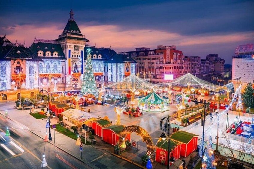 A festive square with illuminated buildings, a Christmas tree, and a carousel. 2