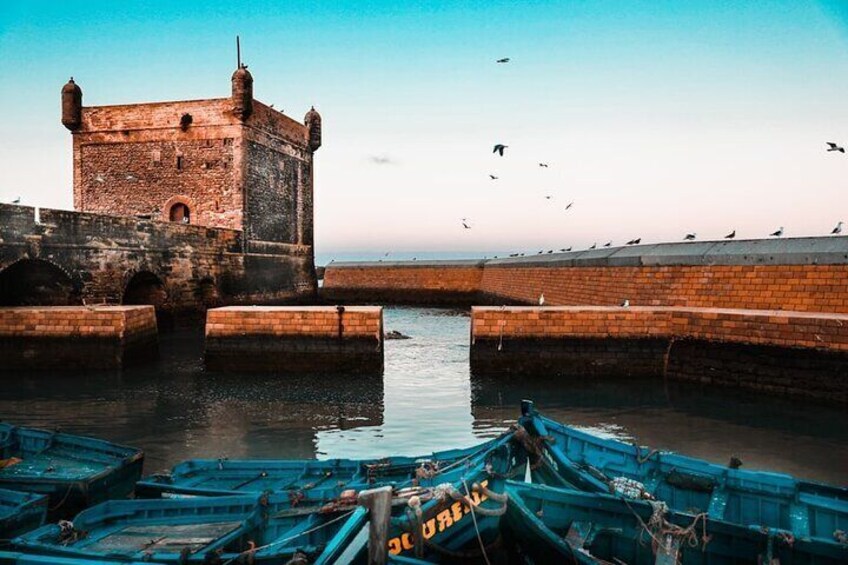 A historic stone tower, a calm waterway, and several boats docked at the pier. 3