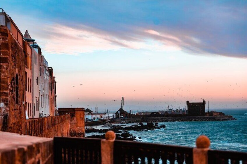 A coastal cityscape with historic buildings, a pier, and a lighthouse. 4