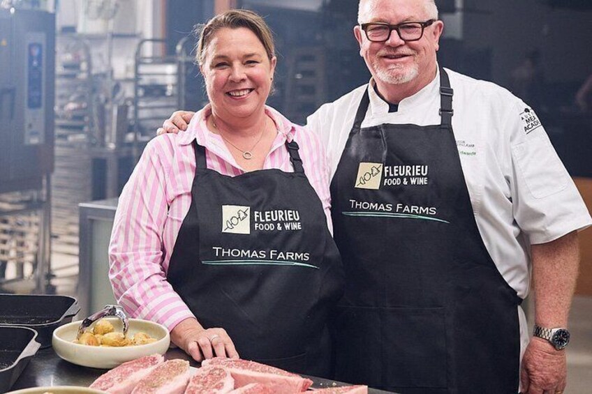 Two people wearing aprons with 'Fleurieu Food & Wine' and 'Thomas Farms' logos, standing in a kitchen with a bowl of food and a cutting board. 4