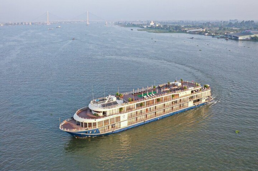 A river cruise ship with multiple decks and a bridge, floating on a river with a distant bridge in the background. 1