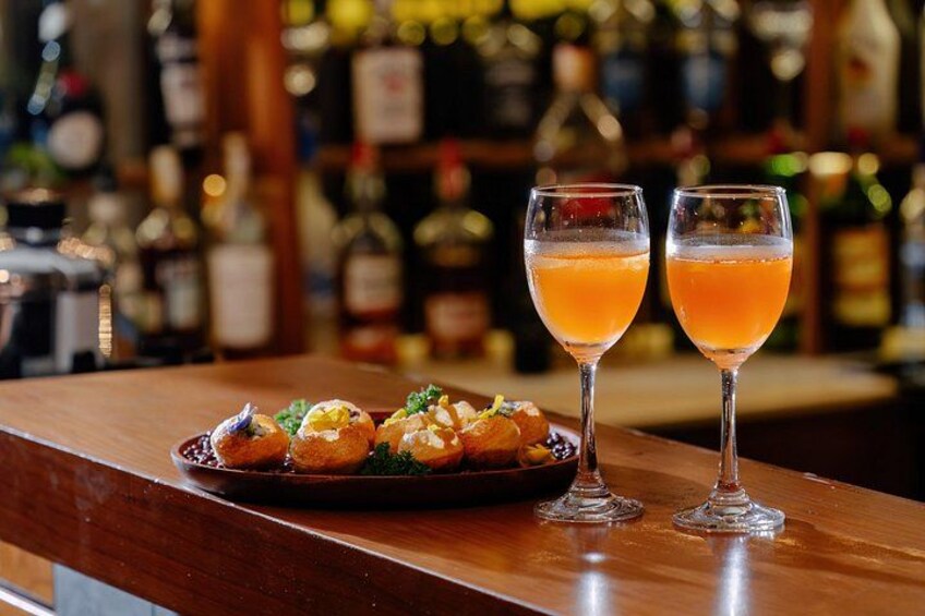 Eine Bar mit zwei Orangencocktails und einem Teller Essen. 2