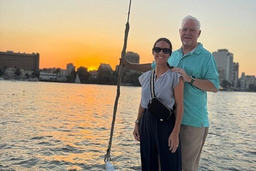 Dos personas de pie junto a un cuerpo de agua, con un atardecer de fondo. 3