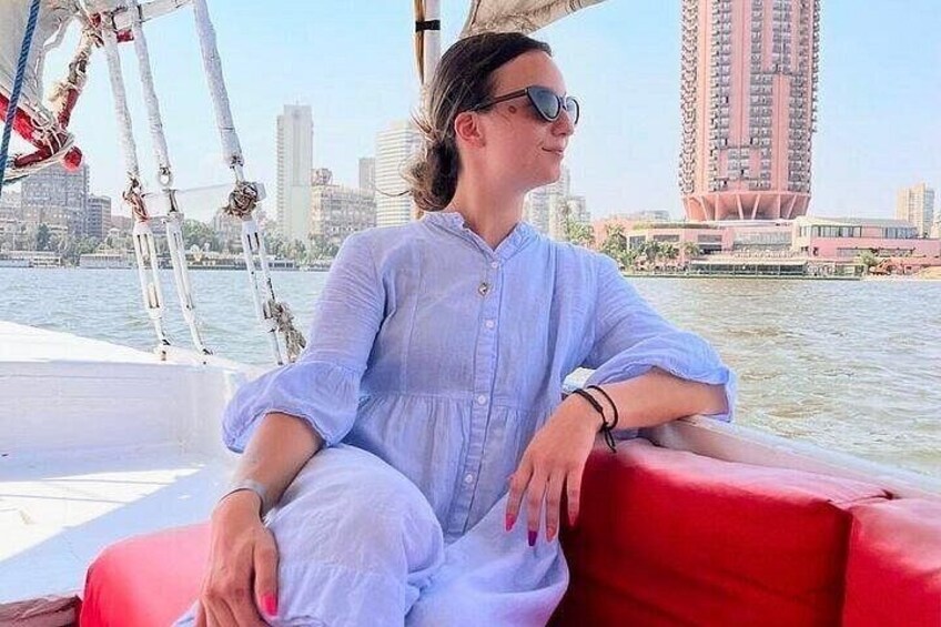 Una persona seduta su un divano rosso su una barca, con lo skyline di una città sullo sfondo. 3