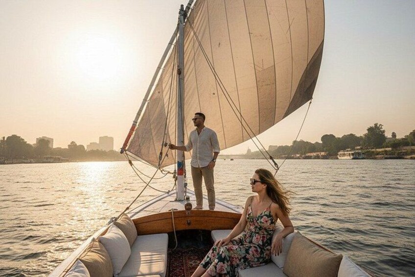 A sailboat with a person standing at the stern and another person seated at the bow, both facing the water. 1