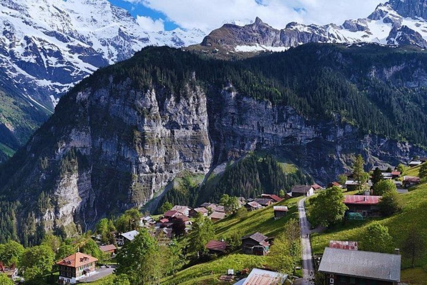 A mountainous village with houses nestled in a valley, surrounded by steep cliffs and snow-capped peaks. 5