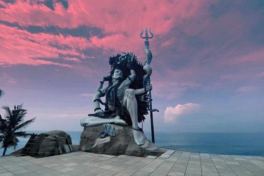 A statue of a deity with a trident, seated on a rock with a backdrop of a pink sky and ocean. 2