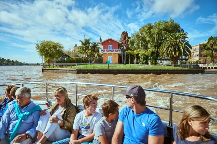 A group of people on a boat with a river and buildings in the background. 1