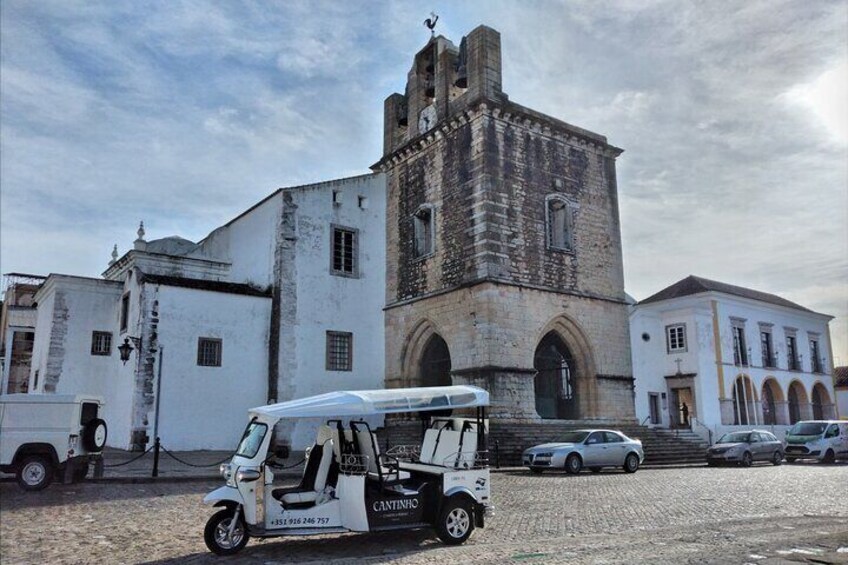 A historic building with a tower, a white van, and parked cars. 1