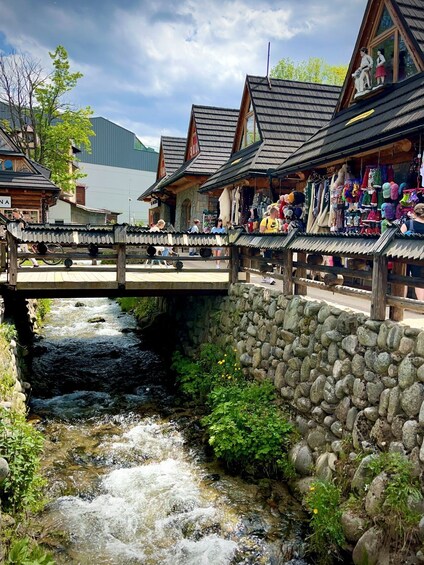 A stone bridge over a flowing river, wooden buildings with traditional architecture, and a clear sky. 2