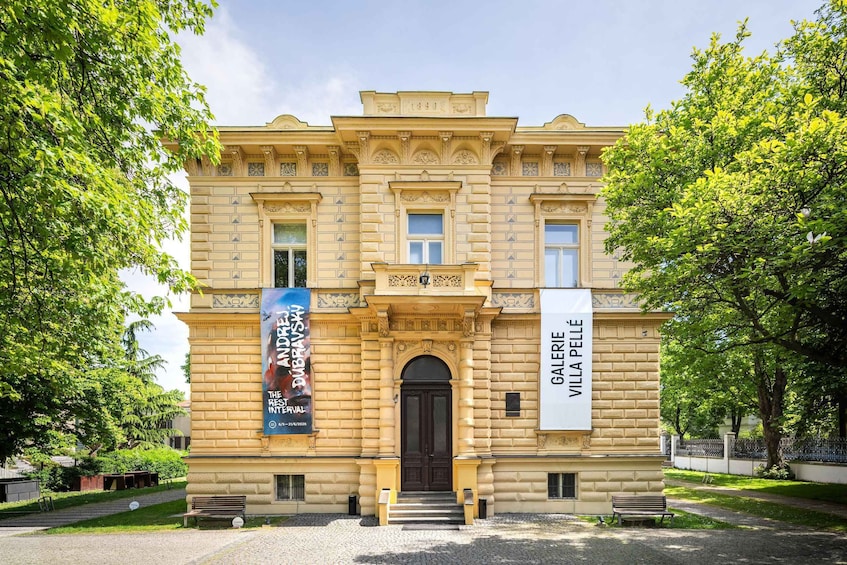 A historic building with ornate architecture, a prominent entrance, and banners advertising an art exhibition. 1