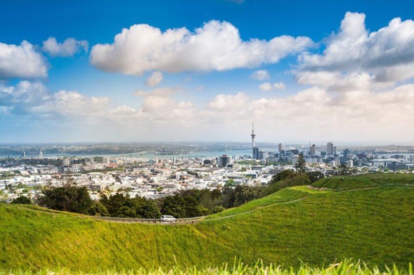 A cityscape with a prominent tower, green fields, and a clear sky. 3