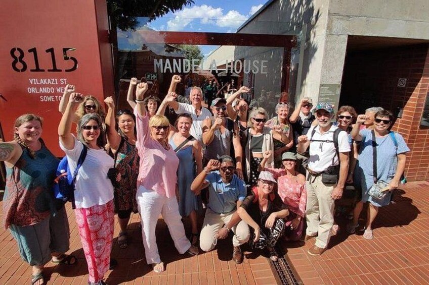 Un groupe de personnes posant devant un bâtiment sur lequel on peut lire l’inscription « Mande House ». 1
