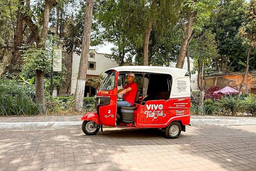 En röd och vit tuk-tuk, märkt med texten ”VIVE Tours”, står parkerad på en asfalterad väg. 4