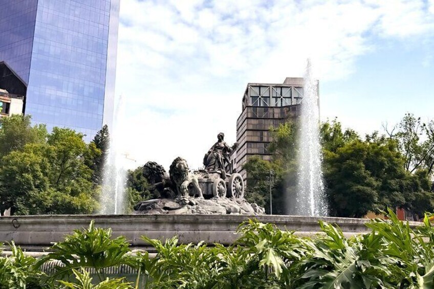A fountain with a statue of a lion and a rider, surrounded by greenery and modern buildings. 5