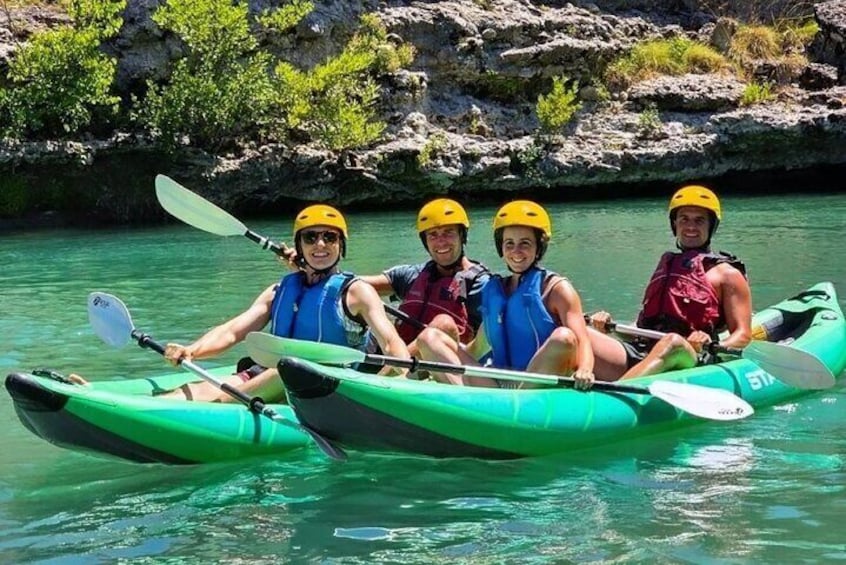 Three people kayaking on a river surrounded by rocky cliffs. 1