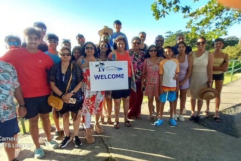 A group of people standing outdoors, some holding a welcome sign. 4