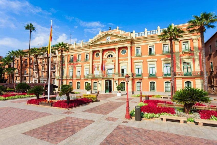 A large, ornate building with a central entrance, surrounded by well-manicured gardens and palm trees. 2
