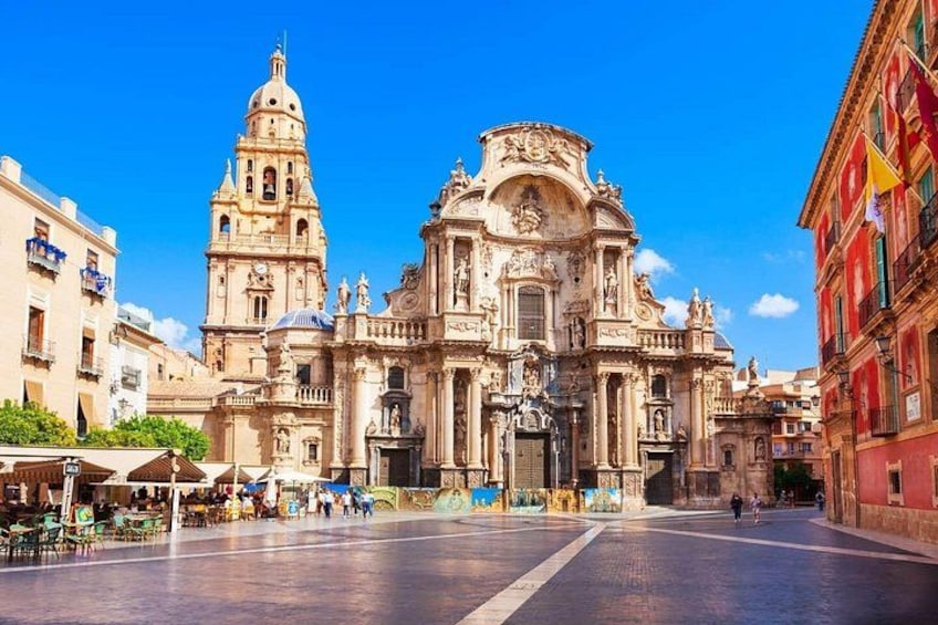 A historic cathedral with intricate architecture, a bell tower, and a plaza with outdoor seating. 1