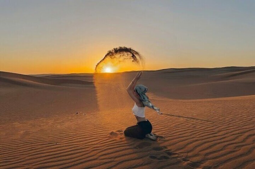 Eine Person in weißem Hemd und schwarzer Hose führt eine Yoga-Pose auf einer Sanddüne bei Sonnenuntergang aus. 1
