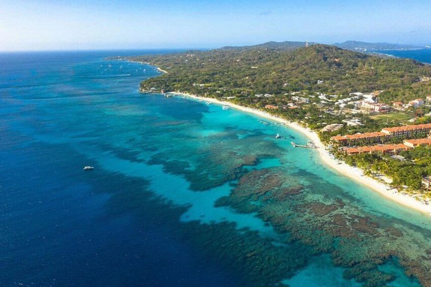 A coastal landscape with a clear blue sea, a sandy beach, and a hilly terrain with vegetation. 2