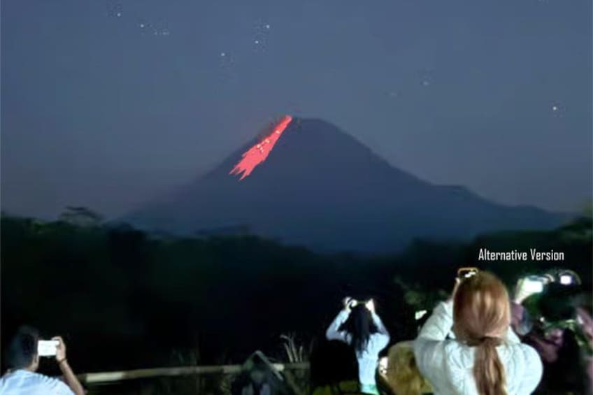 A mountain with a red glow at its peak, possibly from a light or fire, and people taking photos. 3