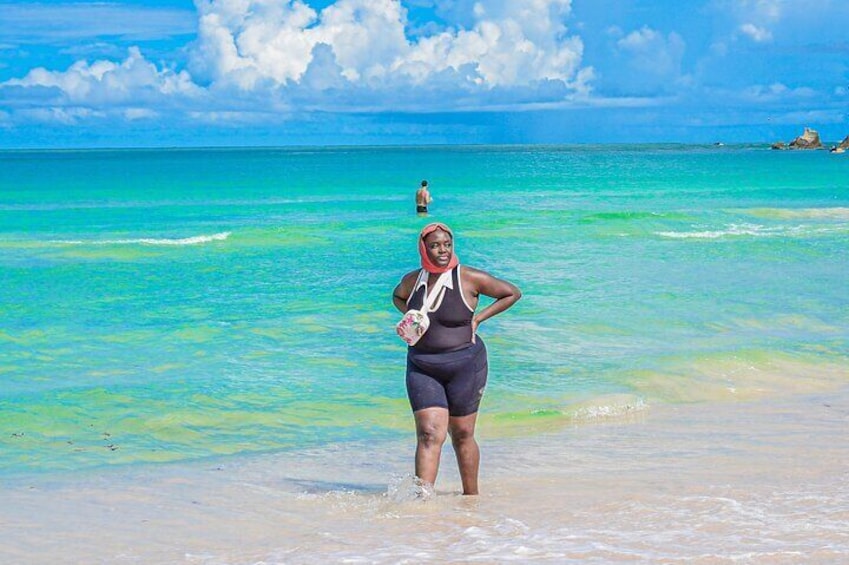 A person standing on a beach with clear turquoise water and a rocky outcrop in the distance. 3