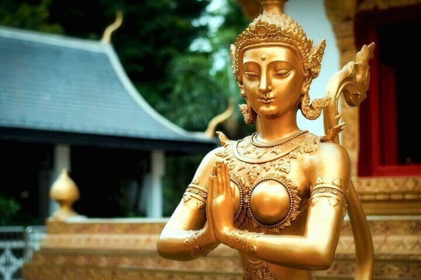 Een gouden beeld van een zittend figuur met handen in een gebedshouding, voor een tempel. 4