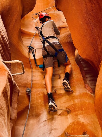 A person climbing a narrow canyon with a helmet and harness. 2
