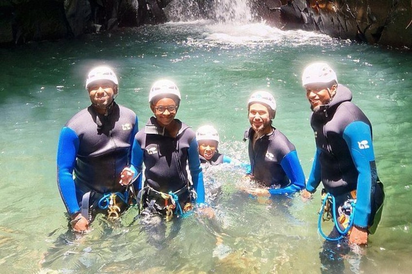A group of people in blue wetsuits and helmets near a waterfall in a clear water body. 2