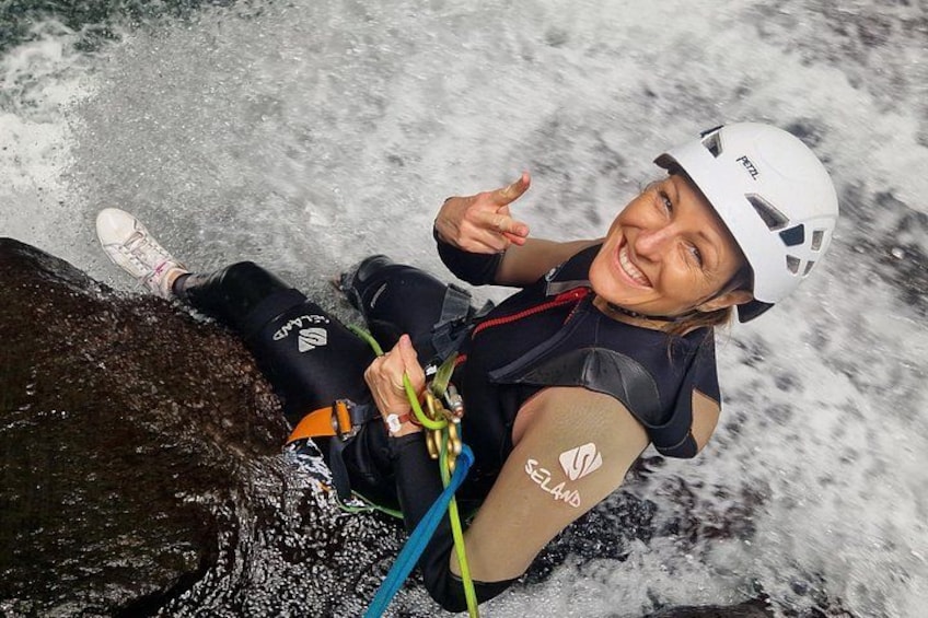 A person in a helmet and wetsuit climbing a rock with a rope. 1