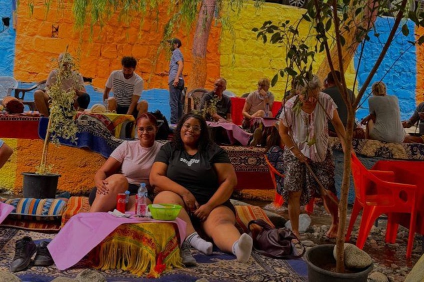 Personas sentadas en esteras y sillas coloridas, con un mural de fondo. 4