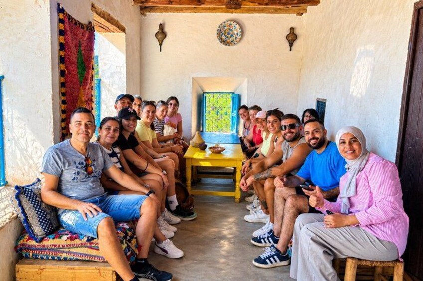 Un groupe de personnes est assis dans une pièce rustique, autour d’une table en bois et entouré de textiles aux couleurs vives. 2