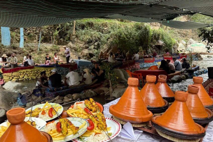 Un ambiente tradicional marroquí con gente sentada bajo un toldo, una mesa con comida y grandes tinajas de barro. 2