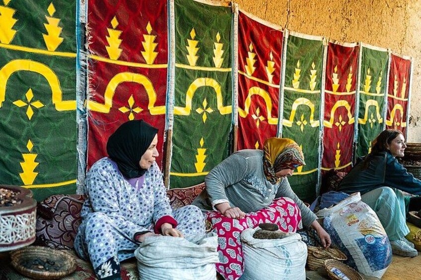 Three women sitting on a bench under a tent with patterned fabric. 4