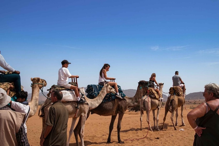A group of people riding camels in a desert landscape. 1
