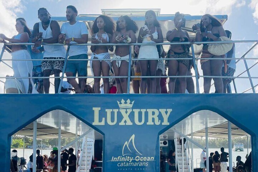 A group of people on a boat with a 'LUXURY' sign and 'Infinity Ocean catamarans' branding. 3