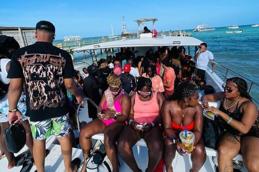A crowded boat with people sitting and standing, a clear blue sky, and the ocean in the background. 4