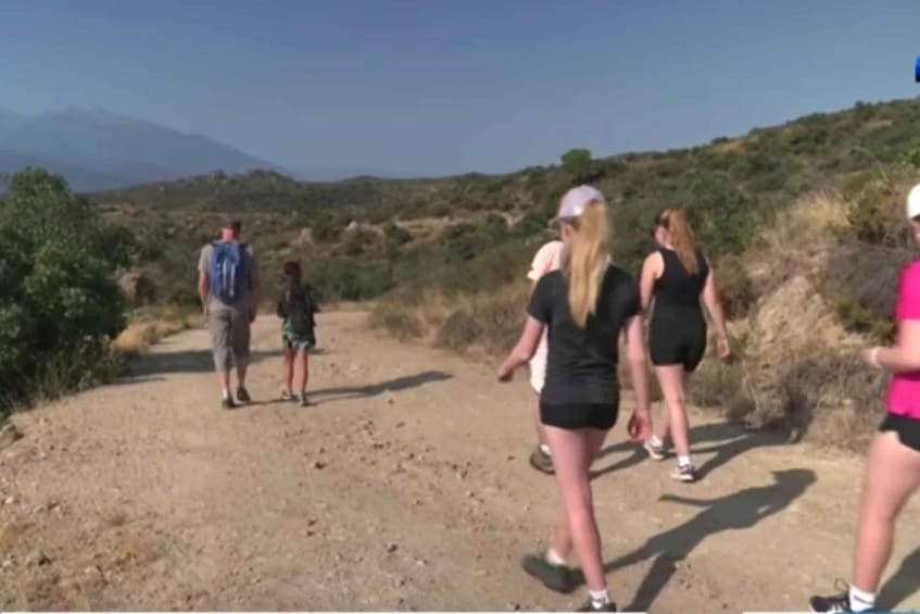 A group of people hiking on a dirt trail surrounded by dry vegetation and hills. 5