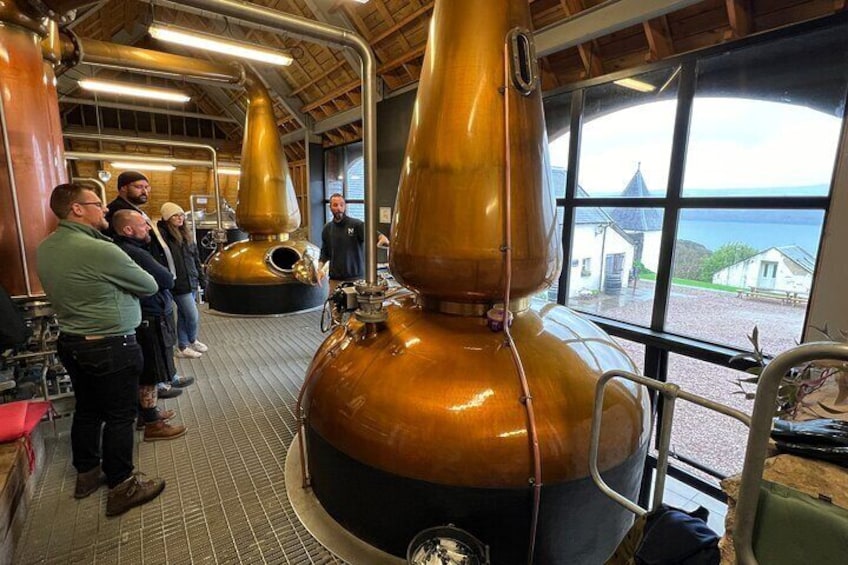 A distillery with large copper stills and a view of the sea through large windows. 2