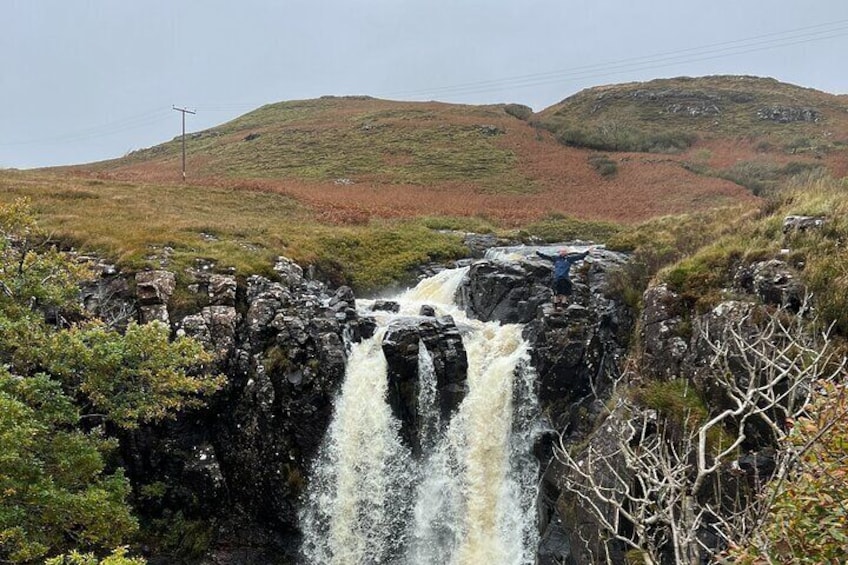 A waterfall cascading over rocks in a hilly landscape. 1