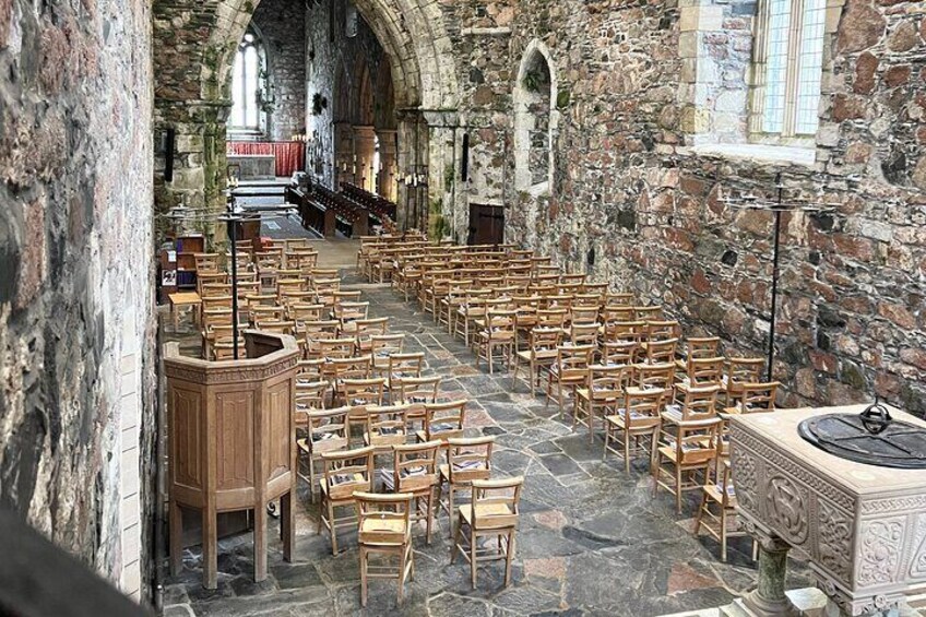 An interior of a historic church with stone walls, wooden pews, and a stone pulpit. 4