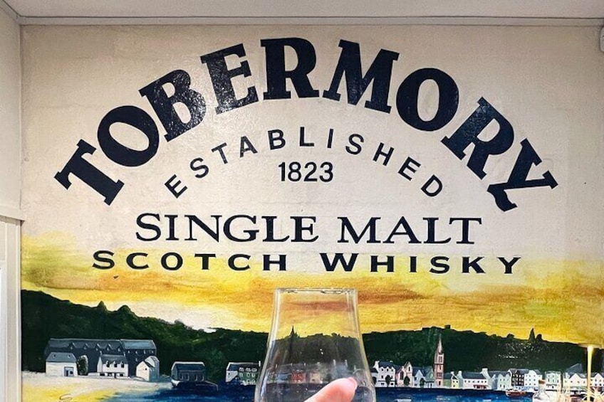 A Tobermory whisky sign with a scenic painting of a town and hills. 5