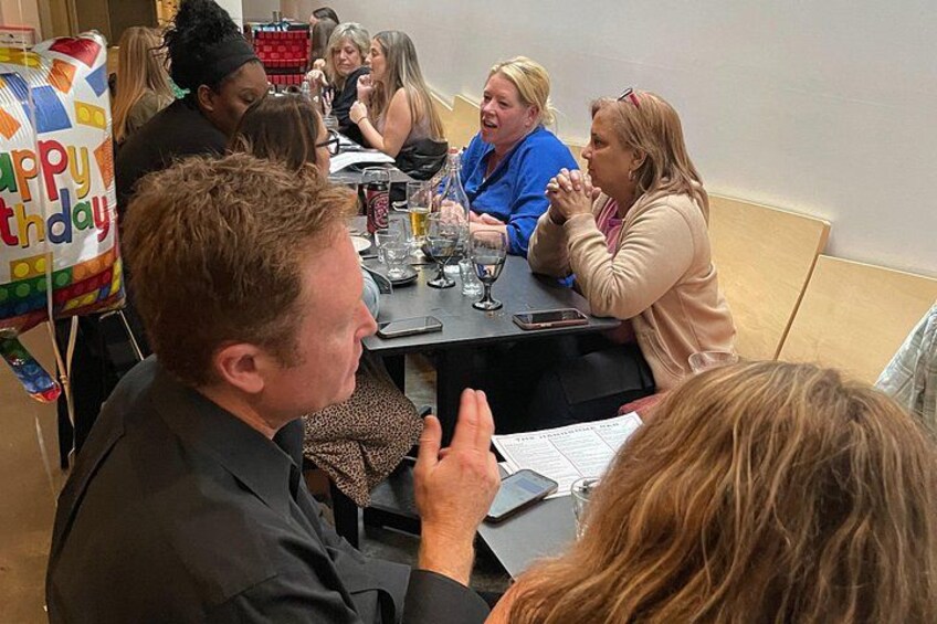A group of people sitting around a table with a birthday balloon. 3