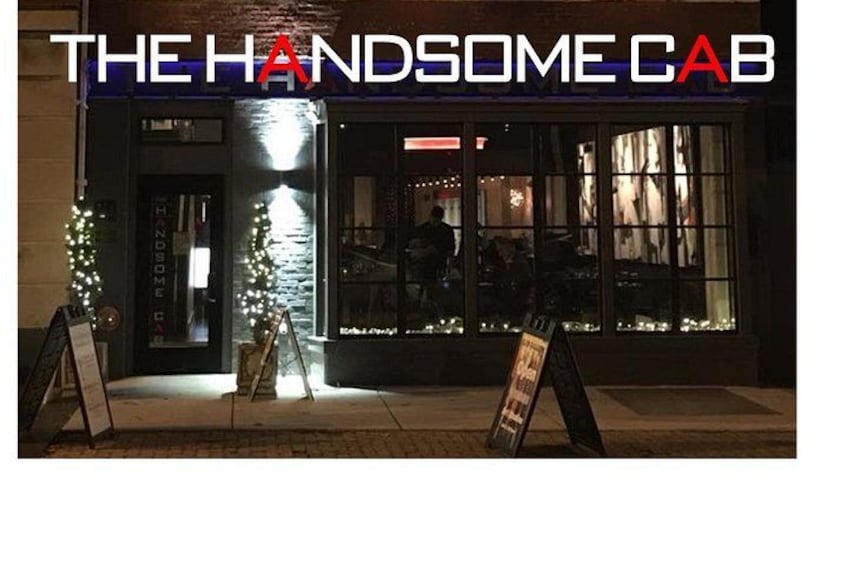 A nighttime view of The Handsome Cab bar with illuminated signage and Christmas decorations. 2