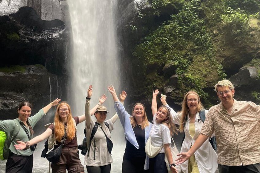 A group of people standing in front of a waterfall with their arms raised. 4